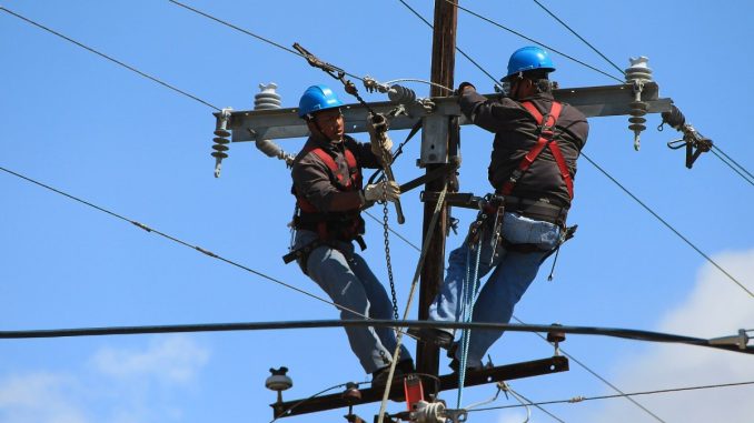Dois eletricistas trabalhando juntos na manutenção de uma linha de energia
